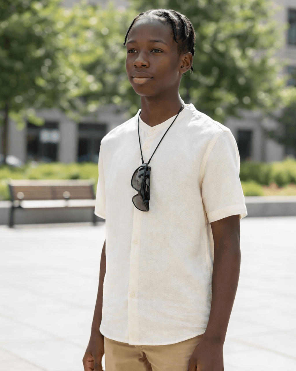 Person wearing a white shirt with sunglasses around their neck, standing outdoors.